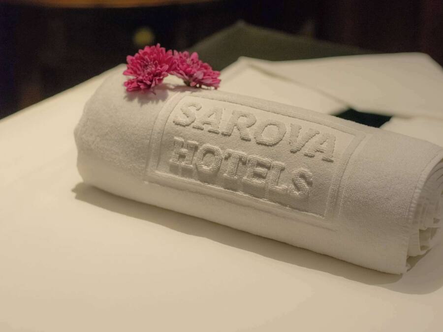 Una toalla blanca doblada con el logotipo de "SAROVA HOTELS" estampado, colocada sobre una cama.
