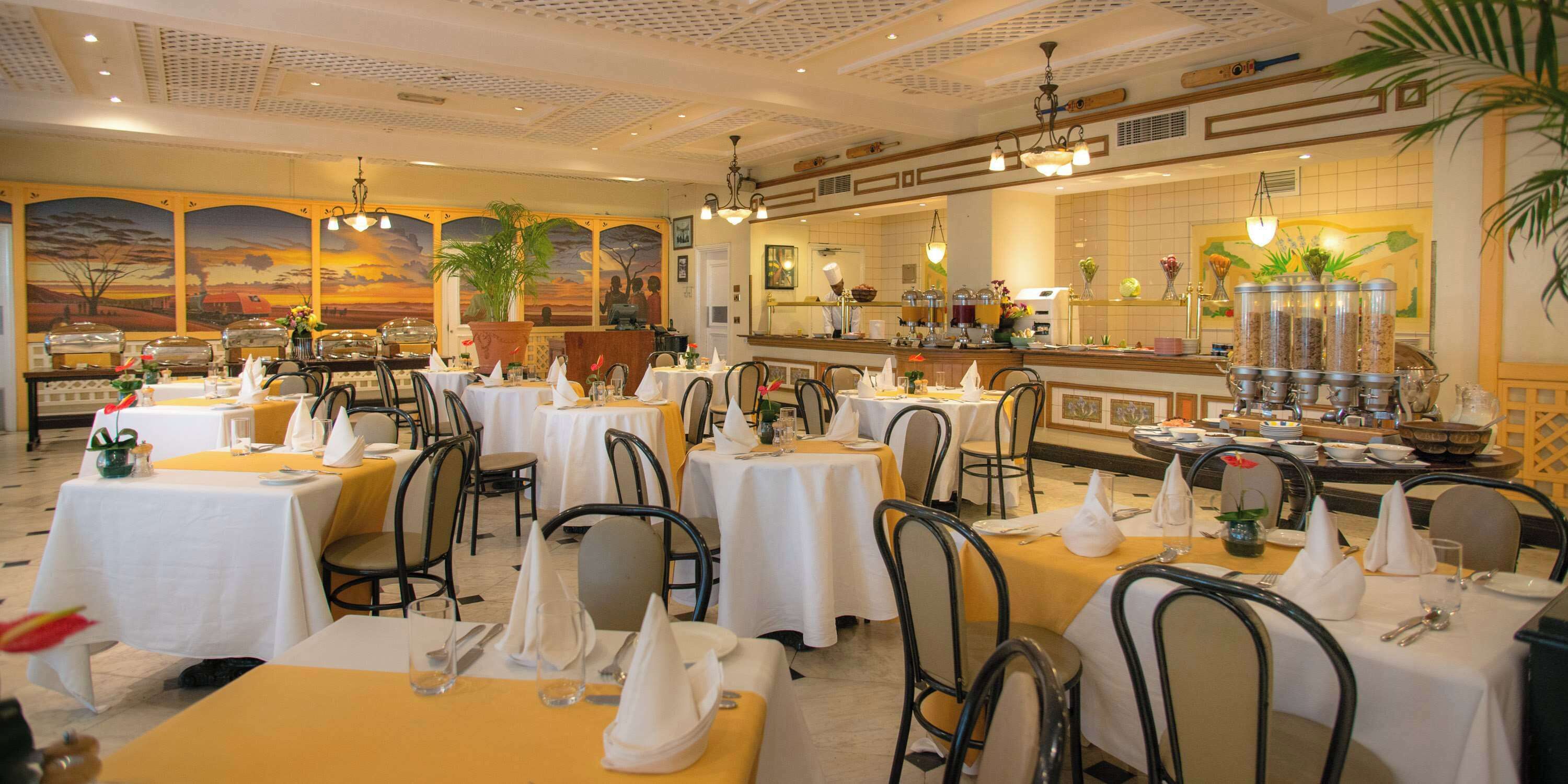 A restaurant with multiple tables set for dining, a bar area, and a mural on the wall.