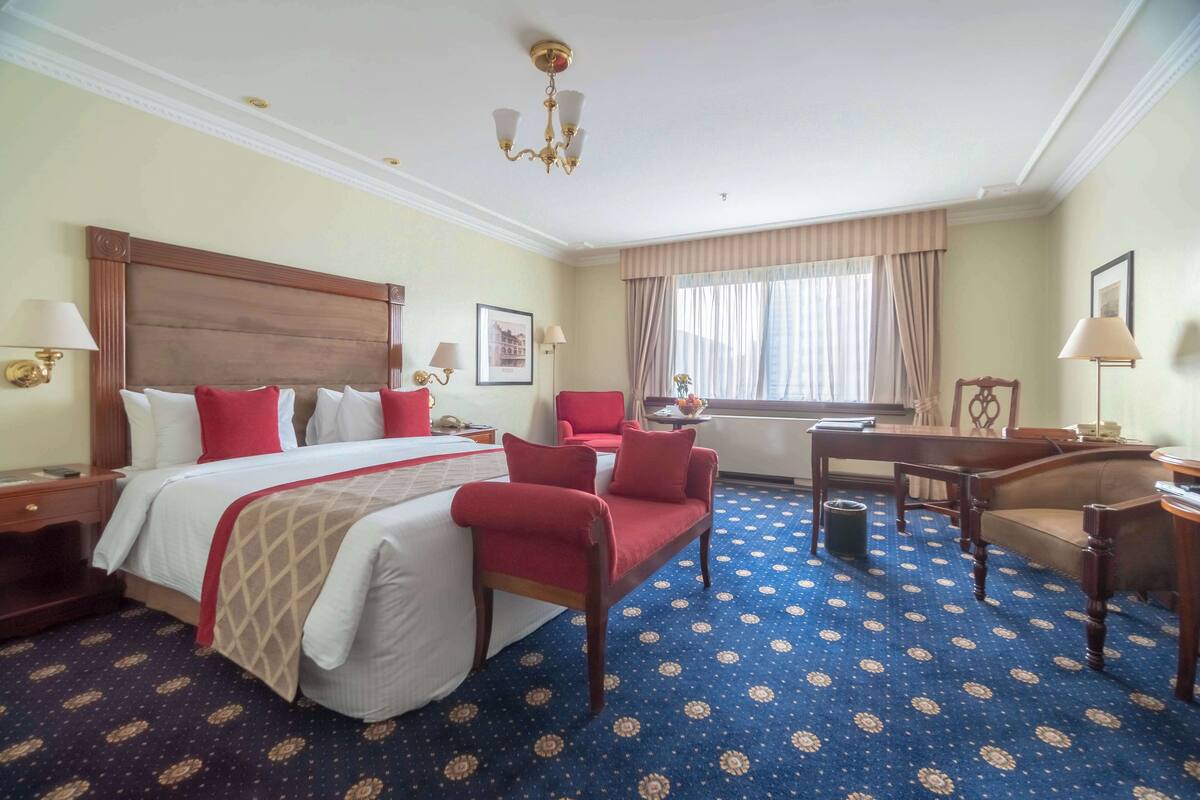 A hotel room with a large bed, a desk, a chair, and a window with curtains.