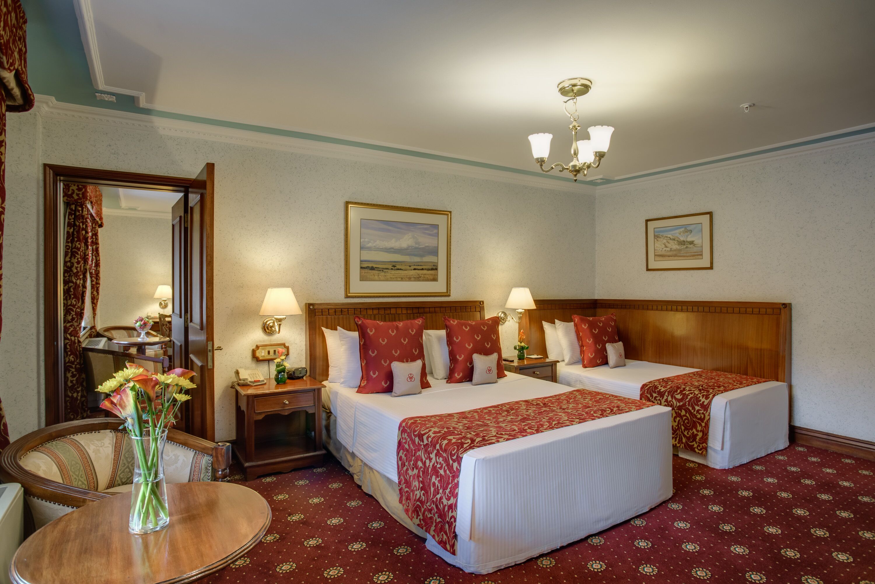 A hotel room with two beds, a round table with a vase of flowers, and a mirror.