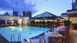 A rooftop pool area with lounge chairs and tables set for dining, overlooking a city skyline at dusk. - Sarova Stanley Hotel, Nairobi (Nairobi)