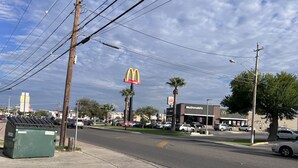 Una vista urbana amb un restaurant McDonald's, palmeres i cotxes aparcats.