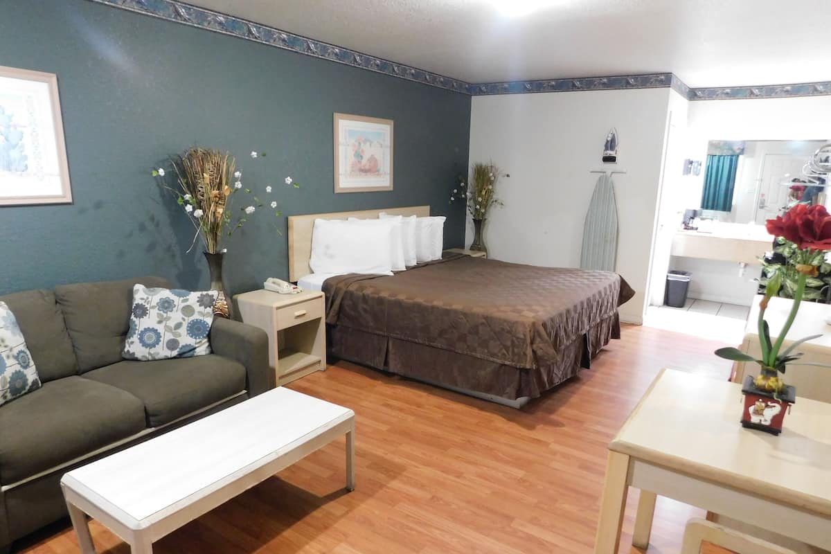 A hotel room with a bed, a sofa, a small table, a nightstand, and a bathroom visible through an open door.