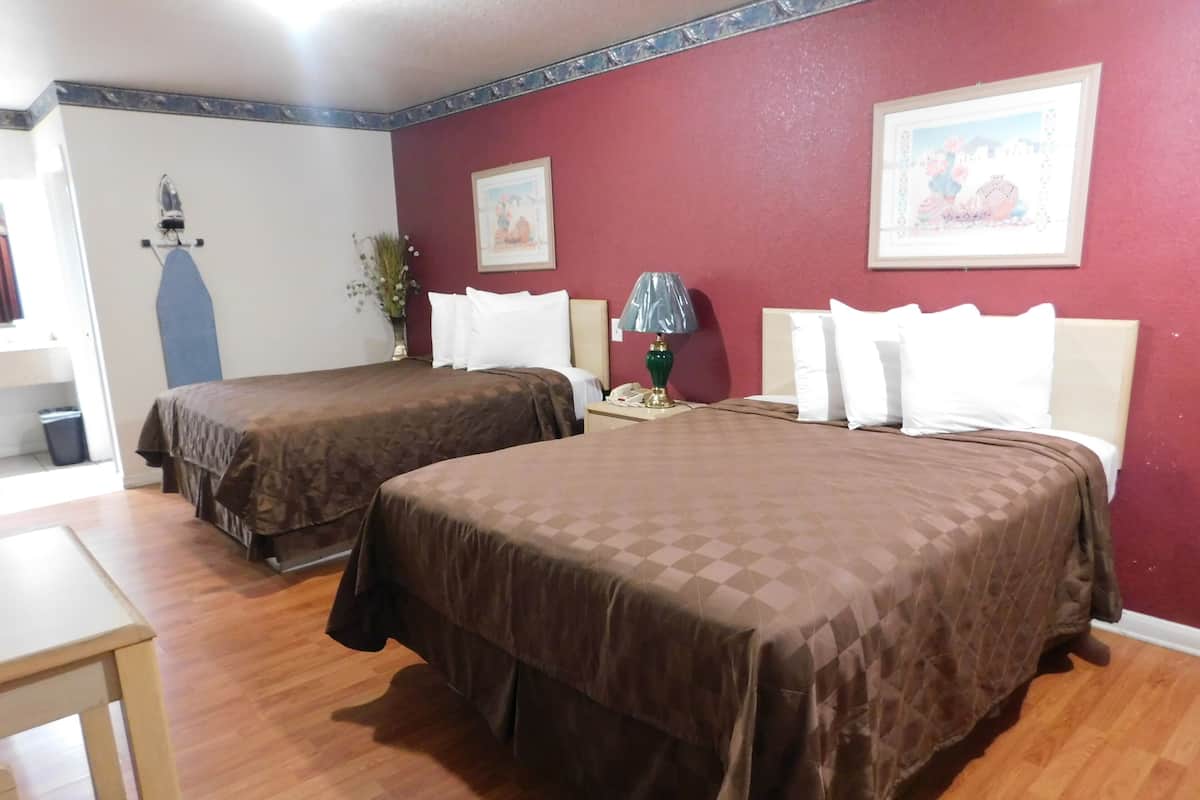 A hotel room with two beds, wooden flooring, a desk, and a lamp.