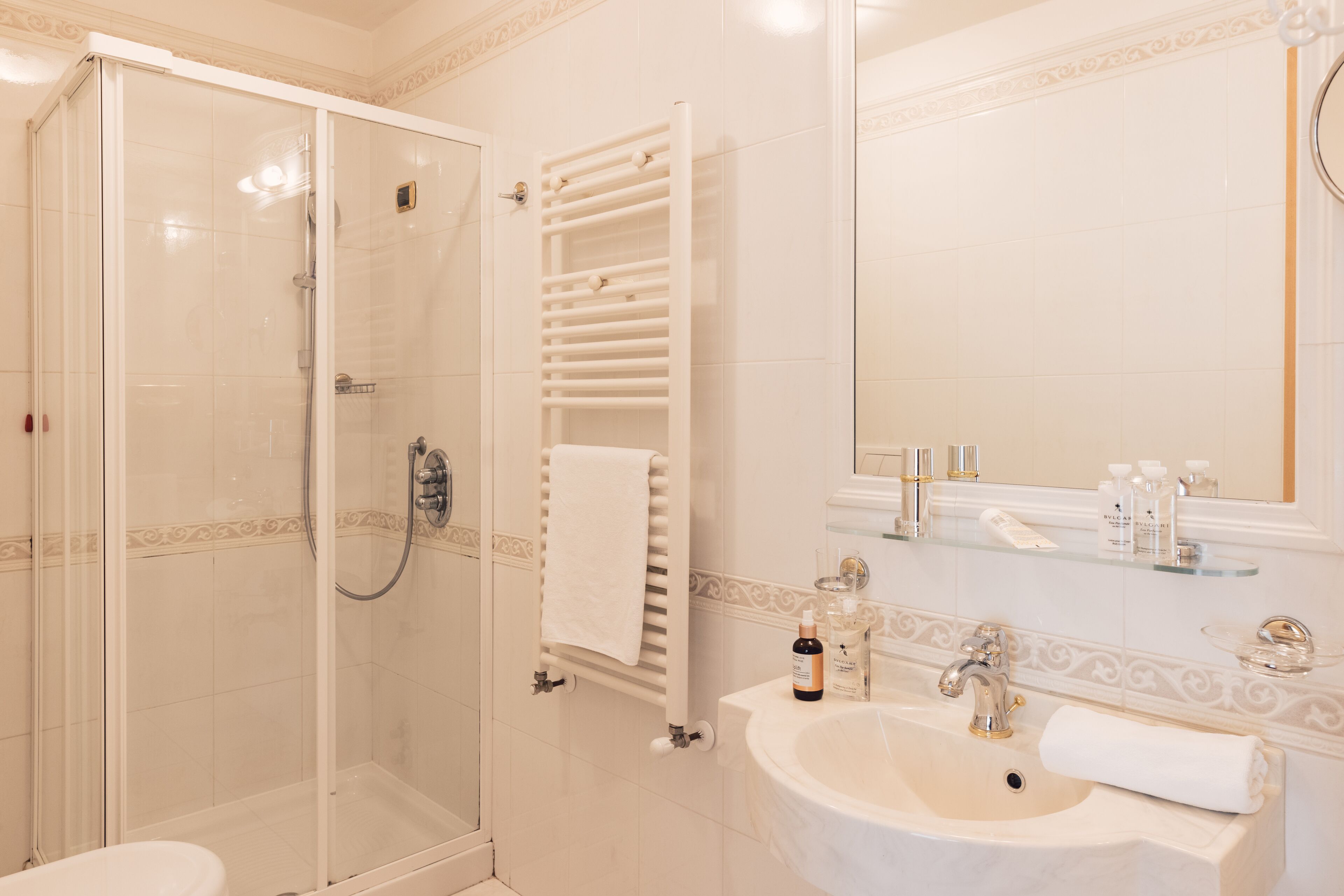 Un bagno con box doccia in vetro, lavandino bianco con specchio sopra e porta asciugamani con un asciugamano.