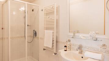Un baño con cabina de ducha de vidrio, un lavabo blanco con un espejo encima y un perchero con una toalla colgada.