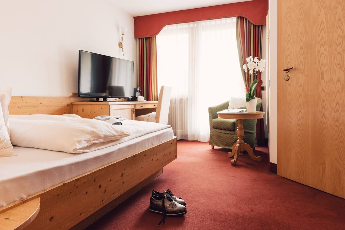 Een hotelkamer met een bed, een televisie, een bureau, een stoel en een kleintje tafeltje met een plant.