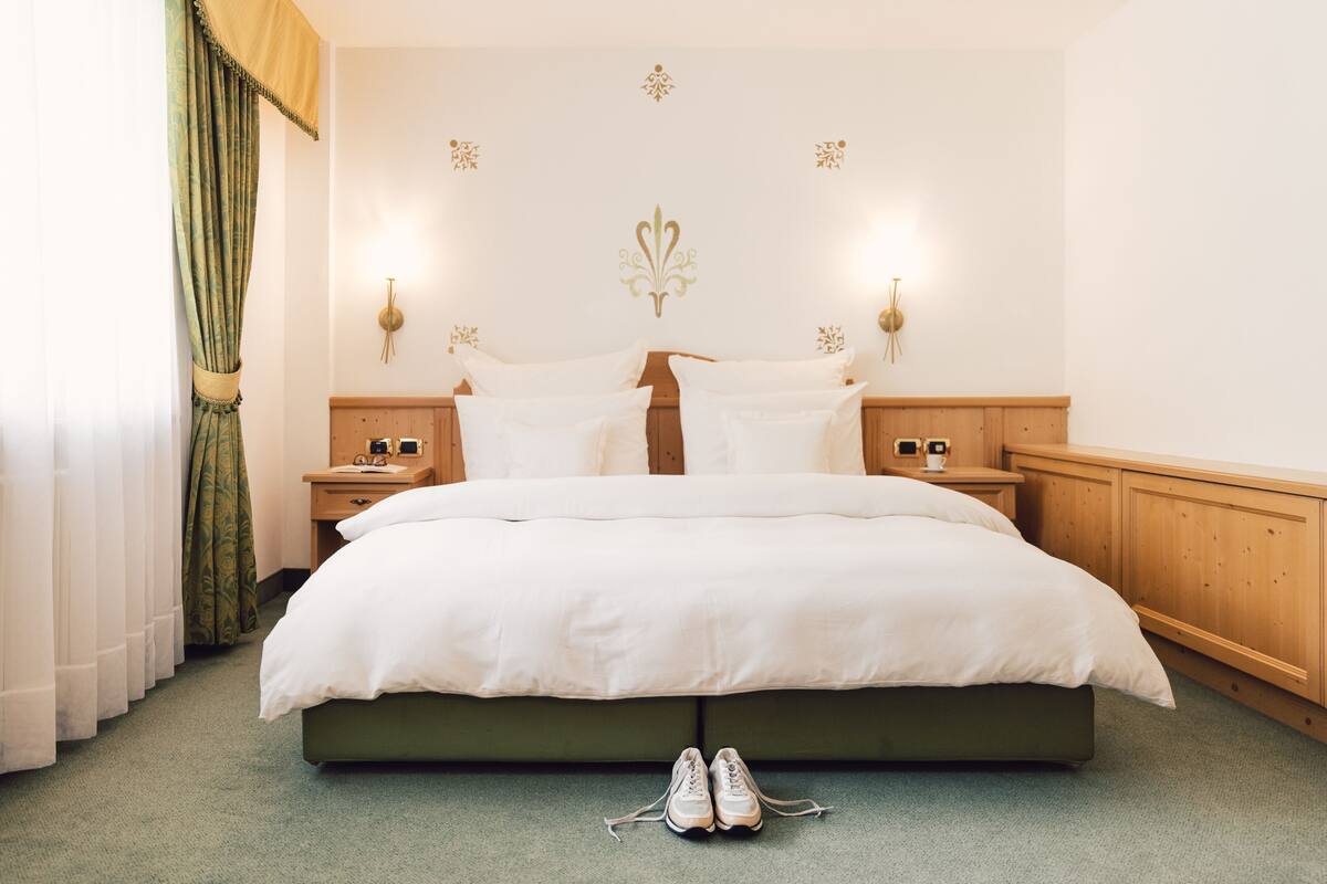Een net opgemaakt bed met witte lakens en een paar schoenen op de vloer.