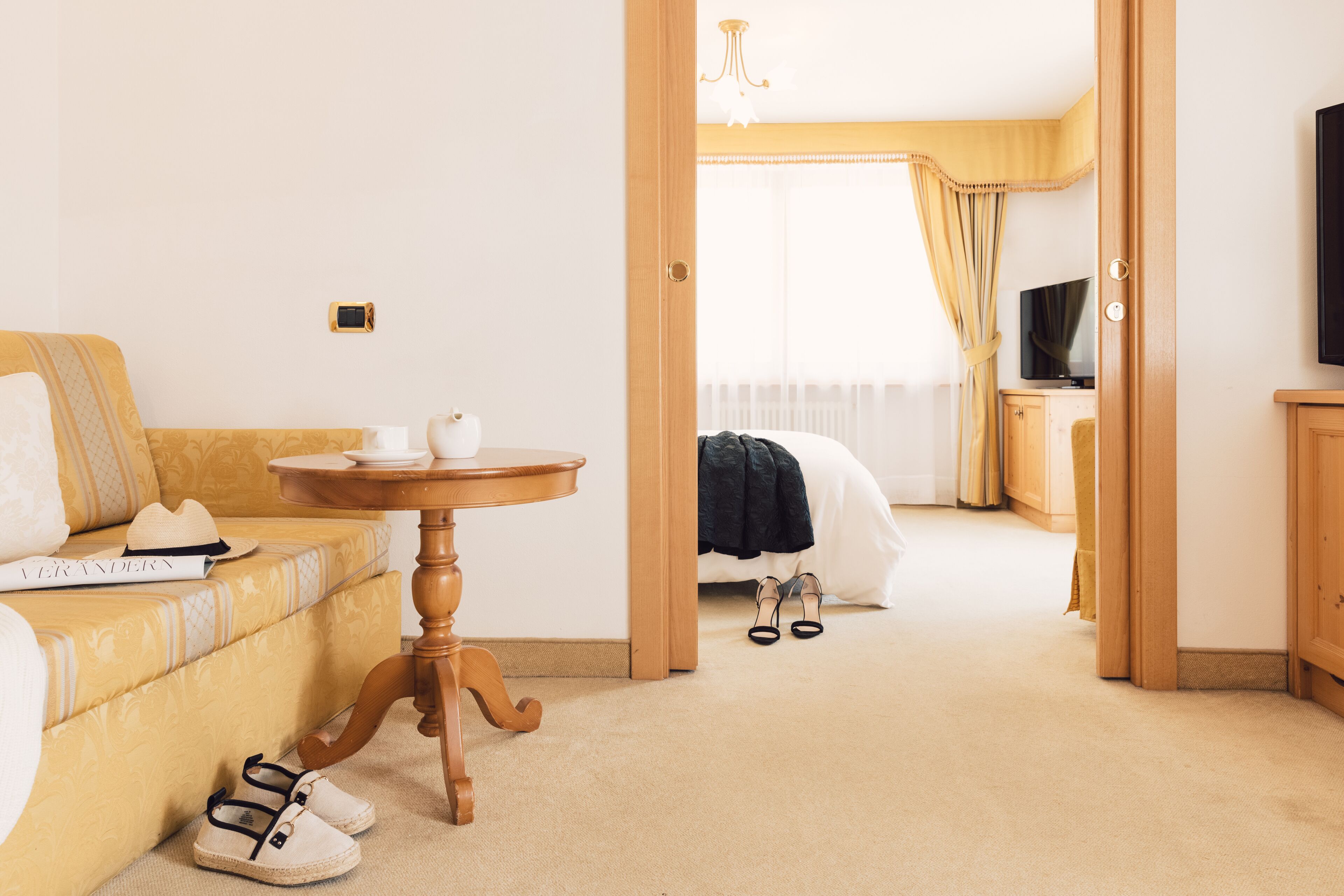 Une chambre d’hôtel avec un canapé, une petite table, une paire de chaussures, une télévision et un lit.