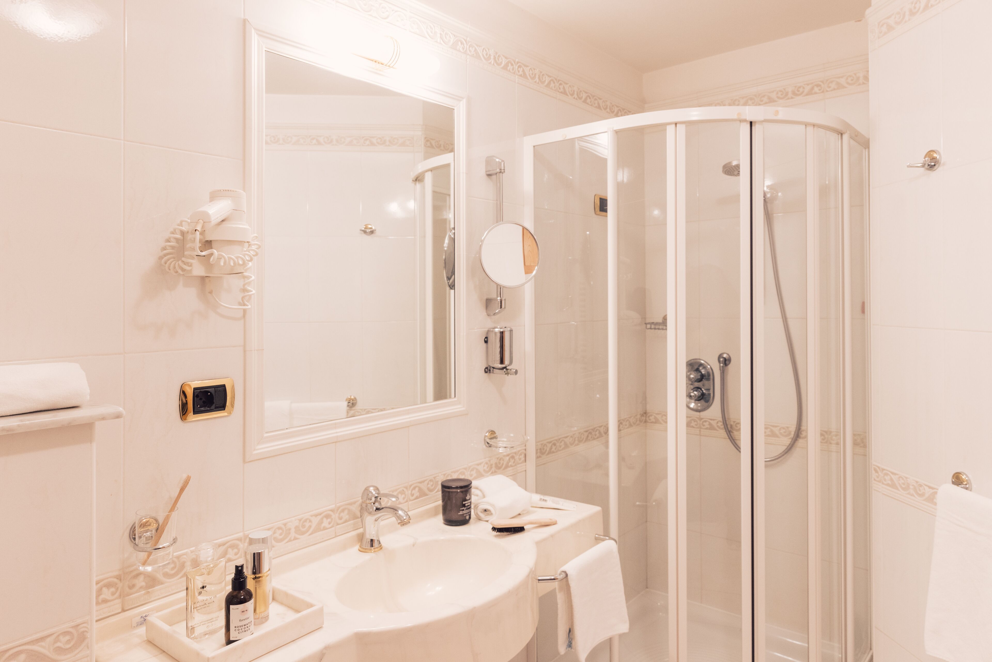 A modern bathroom with a glass-enclosed shower, a large mirror, and a vanity with a sink and toiletries.