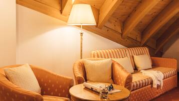 A cozy room with a wooden ceiling, a sofa, a chair, and a small table with a lamp and a glass of water.
