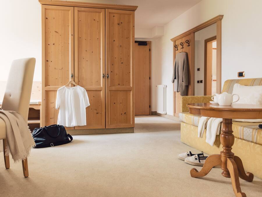 A room with a large wooden wardrobe, a sofa, a small round table, and a chair.