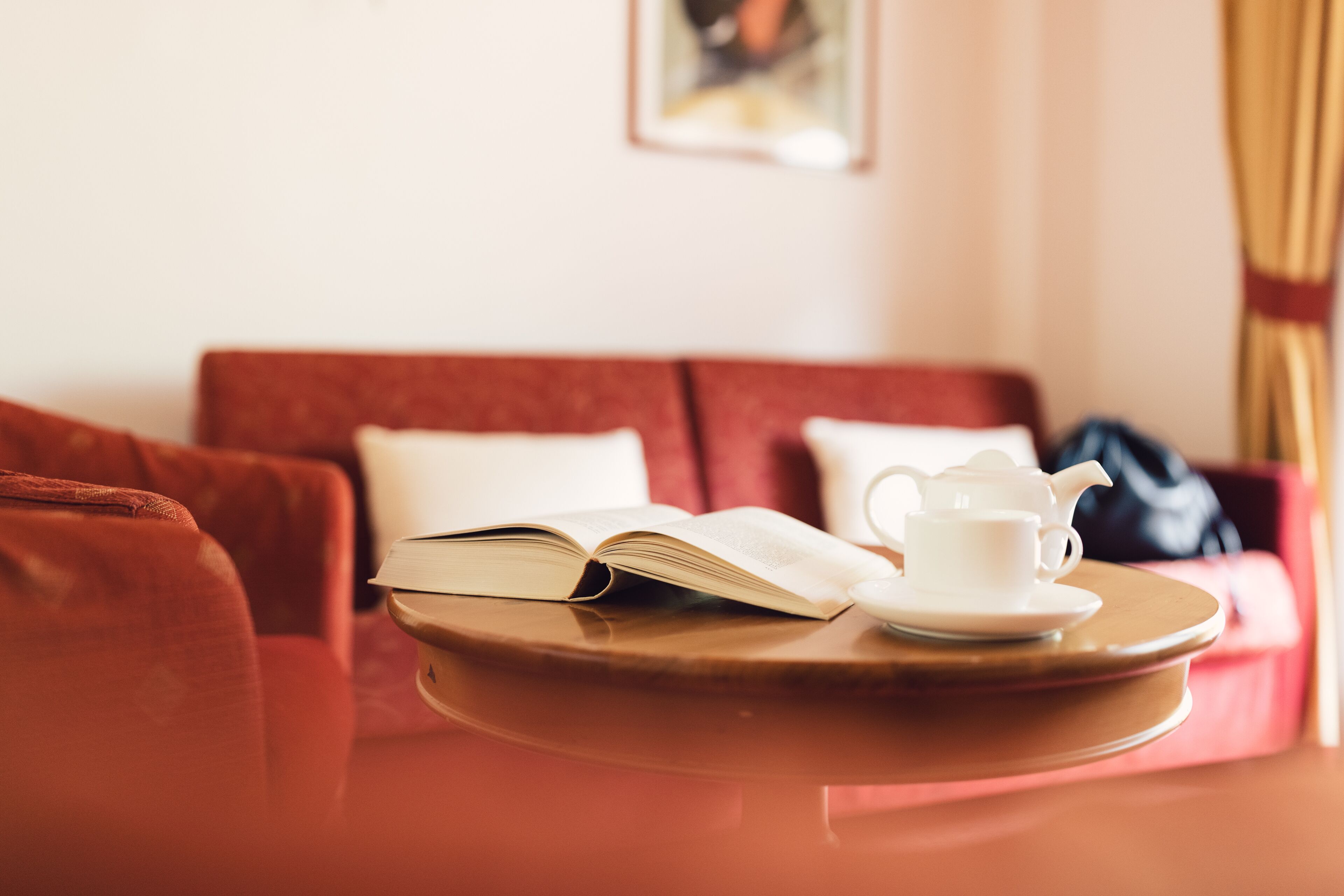 Ein gemütliches Zimmer mit einer roten Couch, einem kleinen Tisch mit Teekanne und Buch.