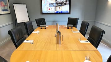 A conference room with a large table, six chairs, a whiteboard, and a television screen displaying a cityscape.