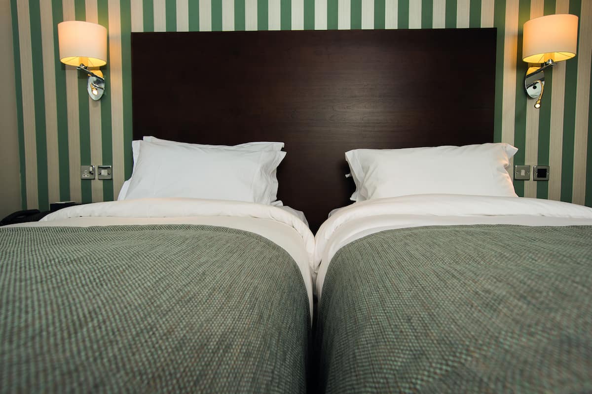Habitación de hotel con dos camas, papel tapiz a rayas y lámparas fijadas a la pared.