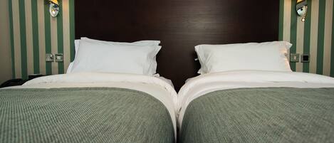 Habitación de hotel con dos camas, papel tapiz a rayas y lámparas fijadas a la pared.