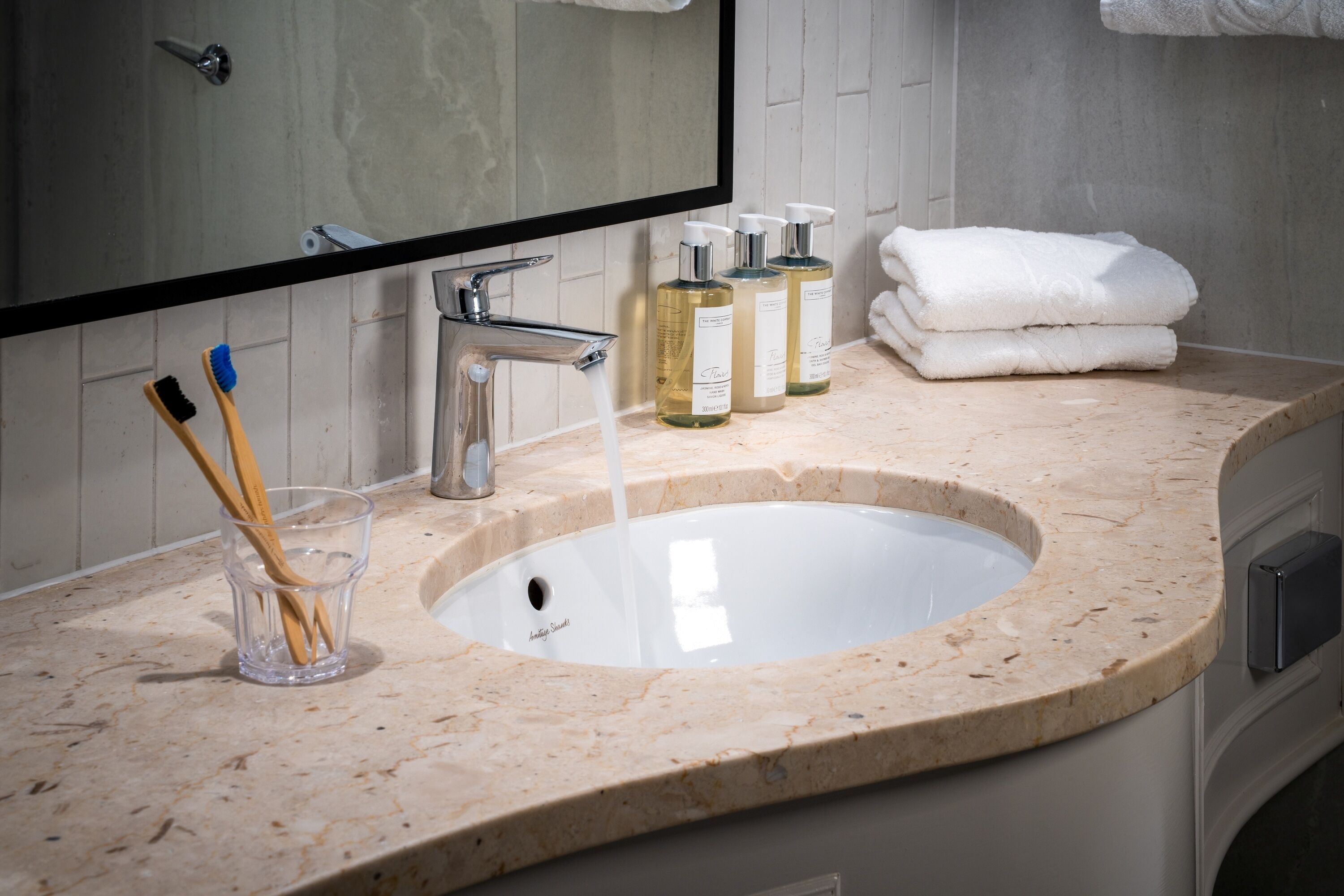 A bathroom with a sink, mirror, toiletries, and towels.