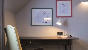 A desk with a lamp, two framed drawings on the wall, and a chair.