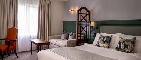 A hotel room with a bed, a chair, a small table, a lamp, and a wall-mounted light fixture.