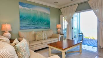 A living room with a large ocean wave painting, a sofa, a coffee table, and a view of the sea through a glass door.