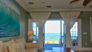 Quarto com vista para o oceano, uma mesa de madeira, um sofá com almofadas florais e um abajur.