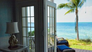 Quarto com vista para o oceano, porta que dá para o exterior, mesa com abajur e duas cadeiras de vime.