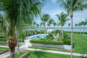 A pool area surrounded by palm trees and a white fence, with a clear view of the water and distant buildings. - Indigo Reef Resort Villas & Marina by KeysCaribbean (Marathon)