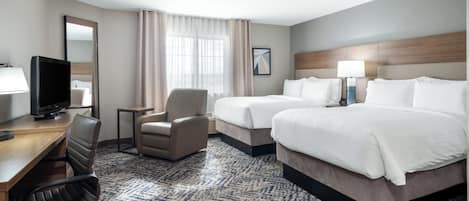 A hotel room with a desk, two beds, a chair, a television, and a window with curtains.