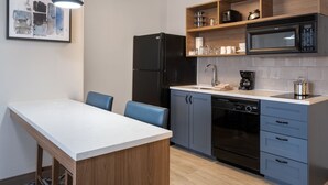 Cozinha moderna com bancada branca, eletrodomésticos pretos e armários azuis.