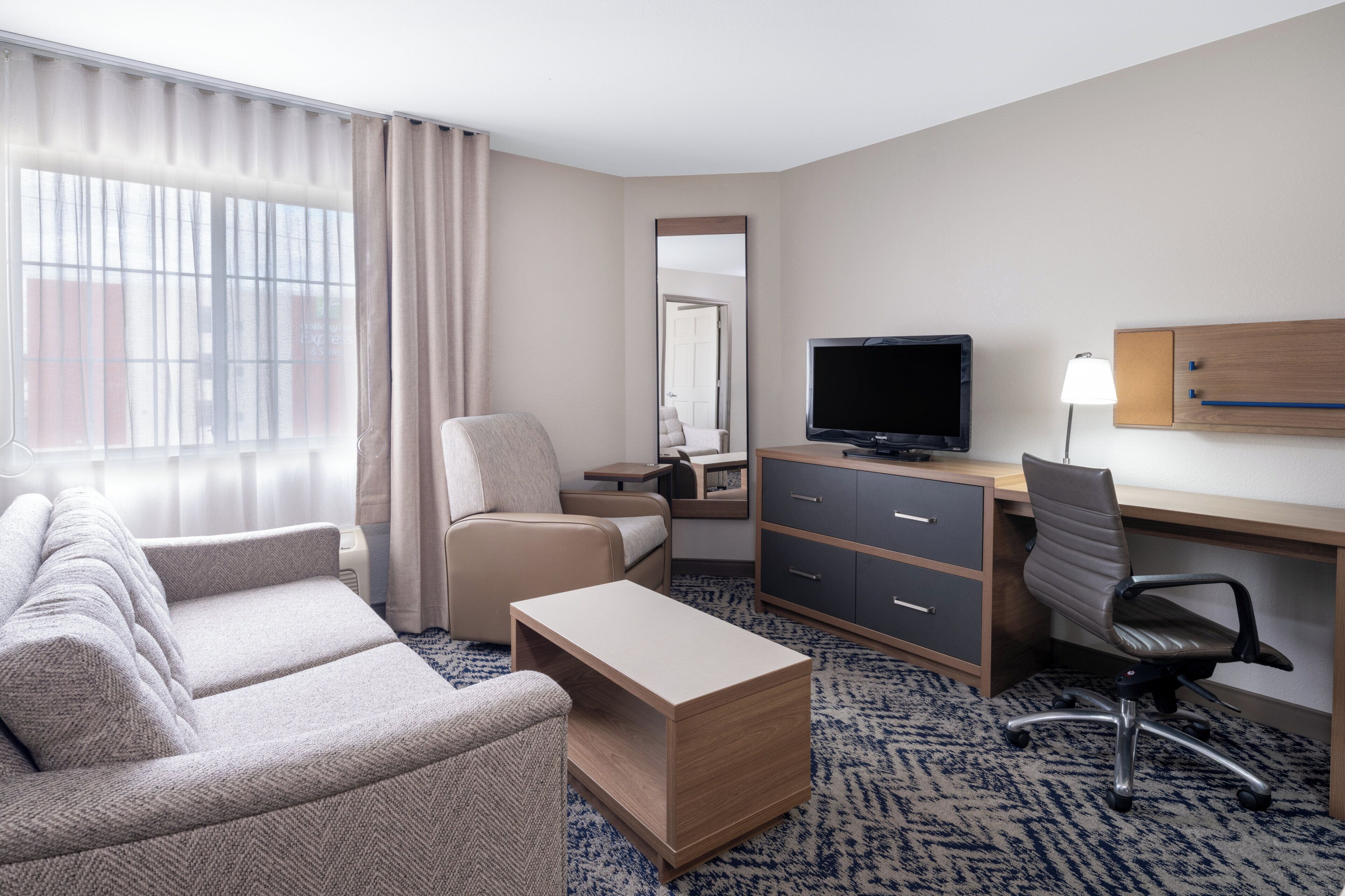 A hotel room with a sofa, a desk with a computer, a television, and a chair.