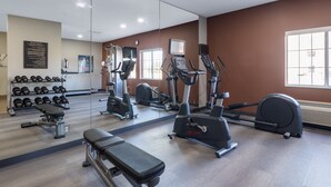 Uma academia com aparelhos de cardio, bancos de musculação e halteres.