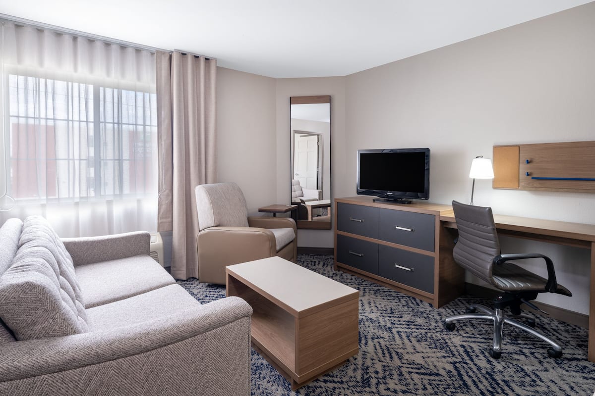 Habitación de hotel con sofá, escritorio, ordenador, televisor y lámpara.