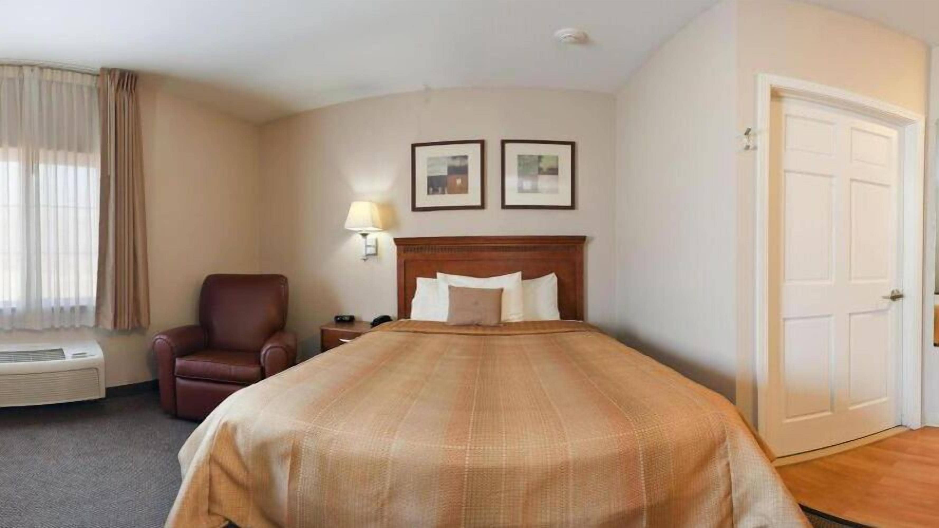 A hotel room with a bed, a chair, a lamp, and a door.
