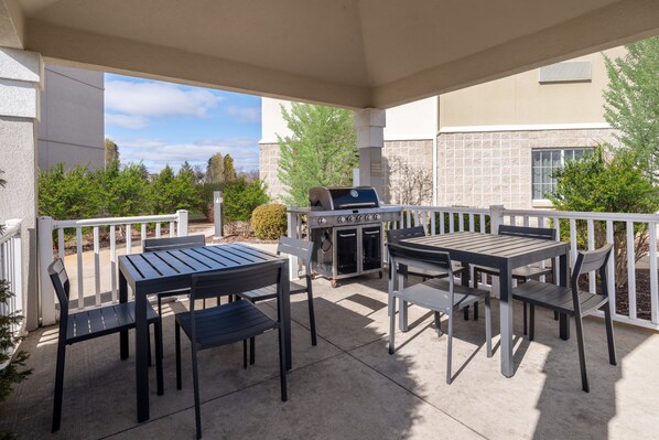 Un patio al aire libre con una parrilla, mesas y sillas.