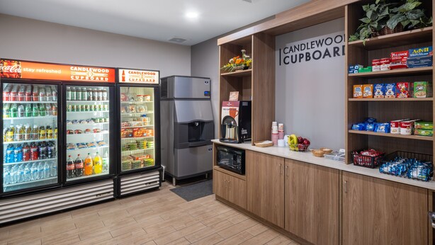 A kitchenette area with a refrigerator, microwave, and coffee maker. There are shelves with snacks and a sign that reads "CANDLEWOOD CUPBOARD".