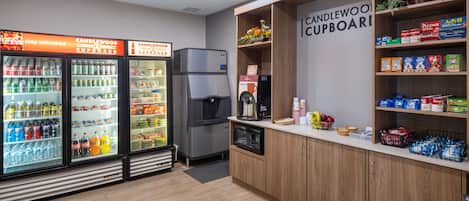 A kitchenette area with a refrigerator, microwave, and coffee maker. There are shelves with snacks and a sign that reads "CANDLEWOOD CUPBOARD".