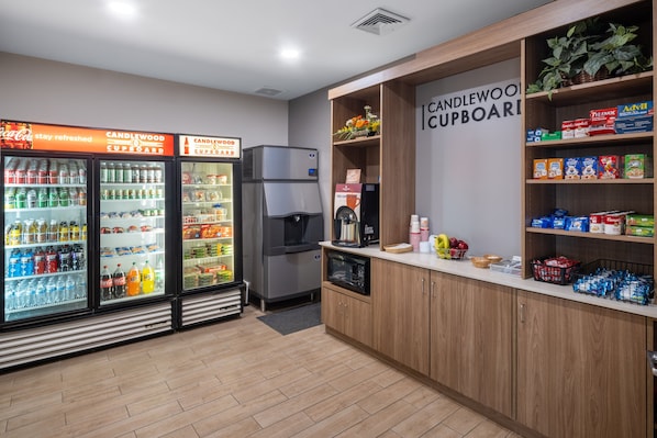 Eine Küchenzeile mit Kühlschrank, Mikrowelle und Kaffeemaschine. Es gibt Regale mit Snacks und ein Schild mit der Aufschrift 'CANDLEWOOD CUPBOARD'.
