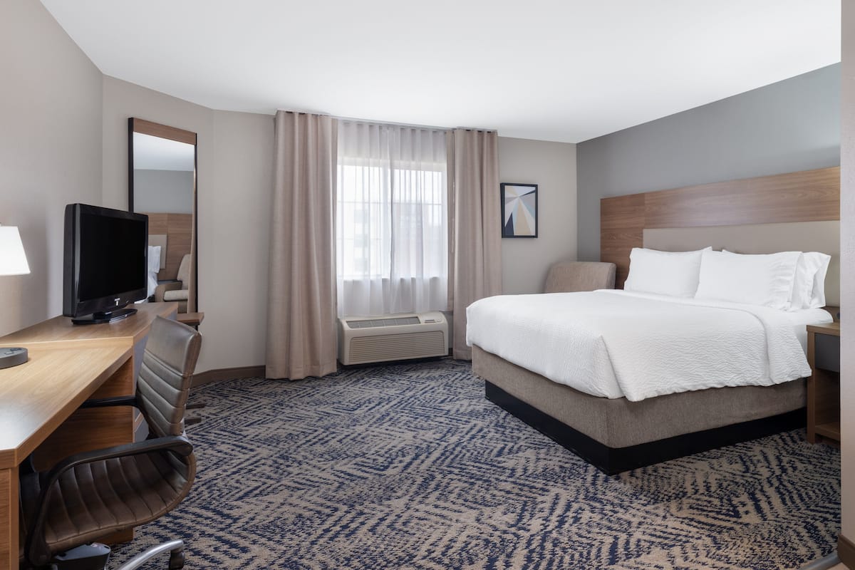 Habitación de hotel con cama, escritorio, silla, televisión, aire acondicionado y ventana con cortinas.