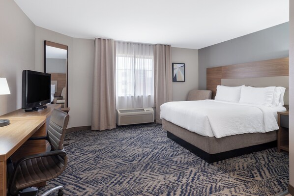 A hotel room with a bed, a desk with a computer, a chair, a television, and a window with curtains.