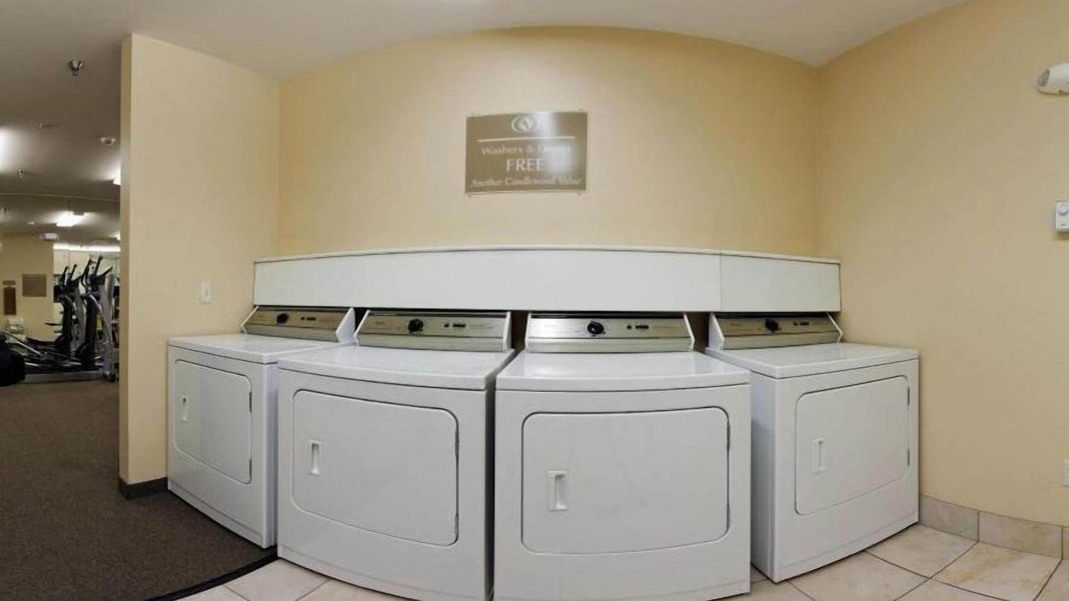 A laundry room with four front-loading washers and dryers, a sign above indicating free use, and a wall-mounted sign.