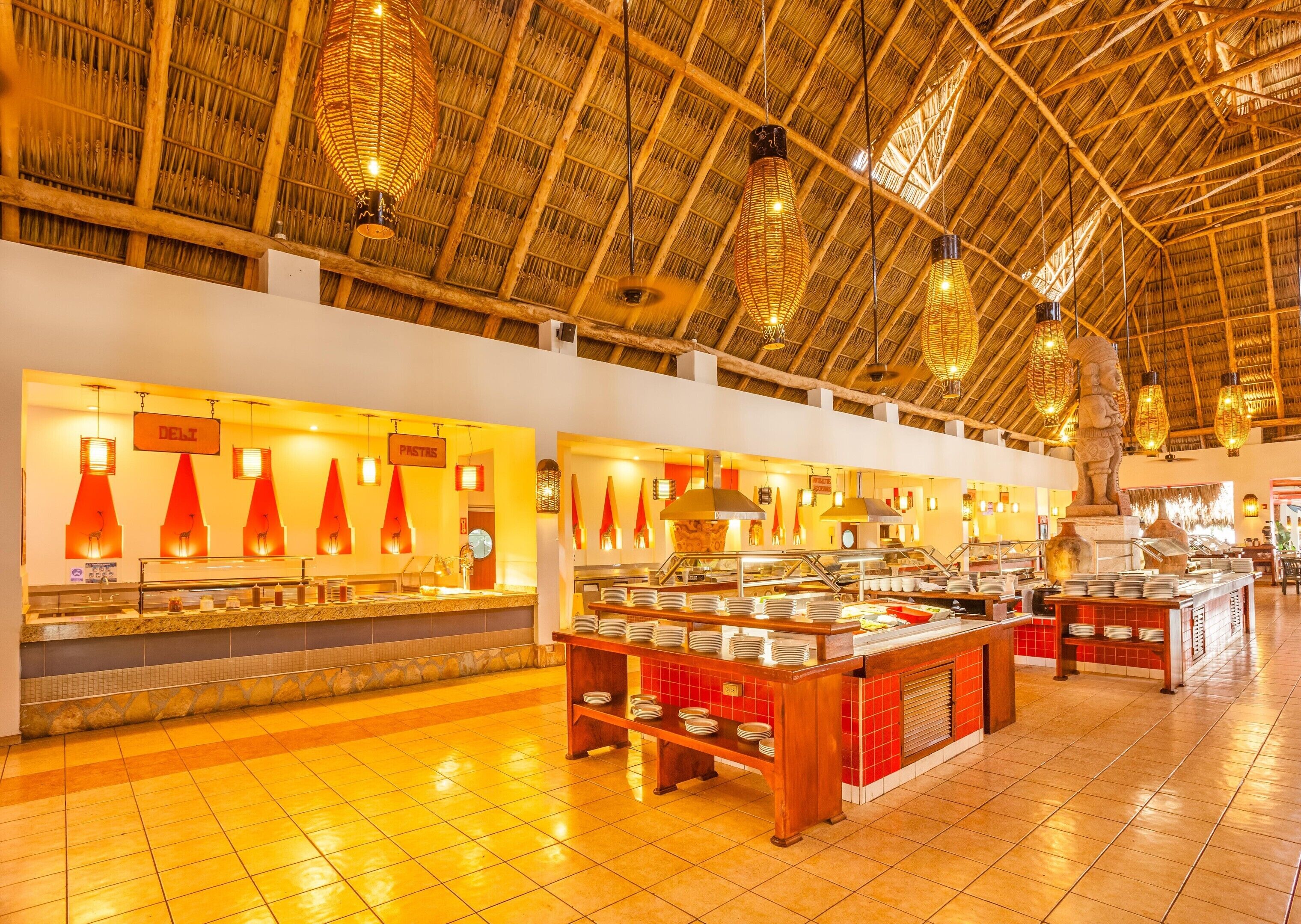 A buffet area with multiple food stations, a thatched roof ceiling, and a tiled floor.