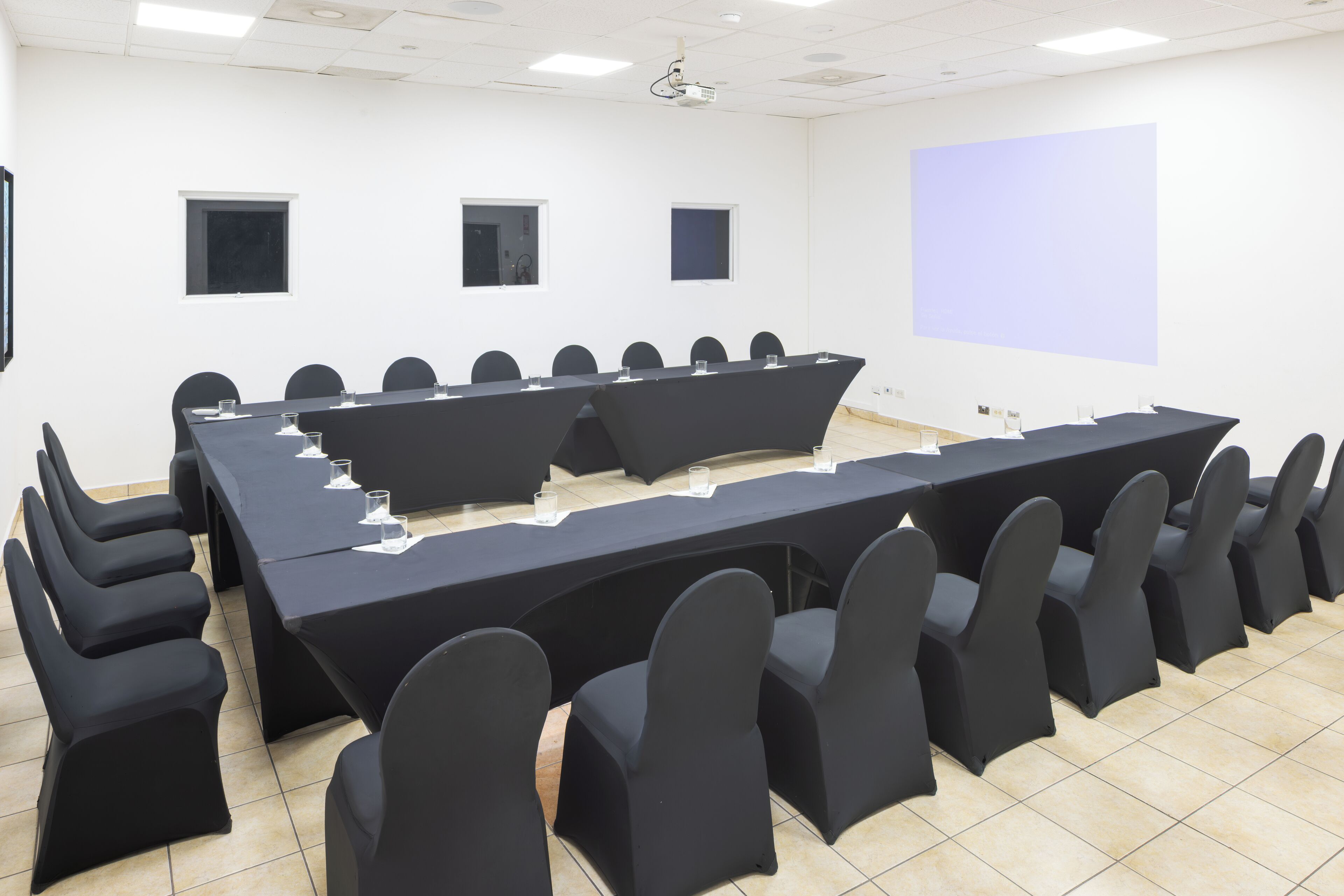 A conference room with a long table, multiple chairs, a projector screen, and a whiteboard.