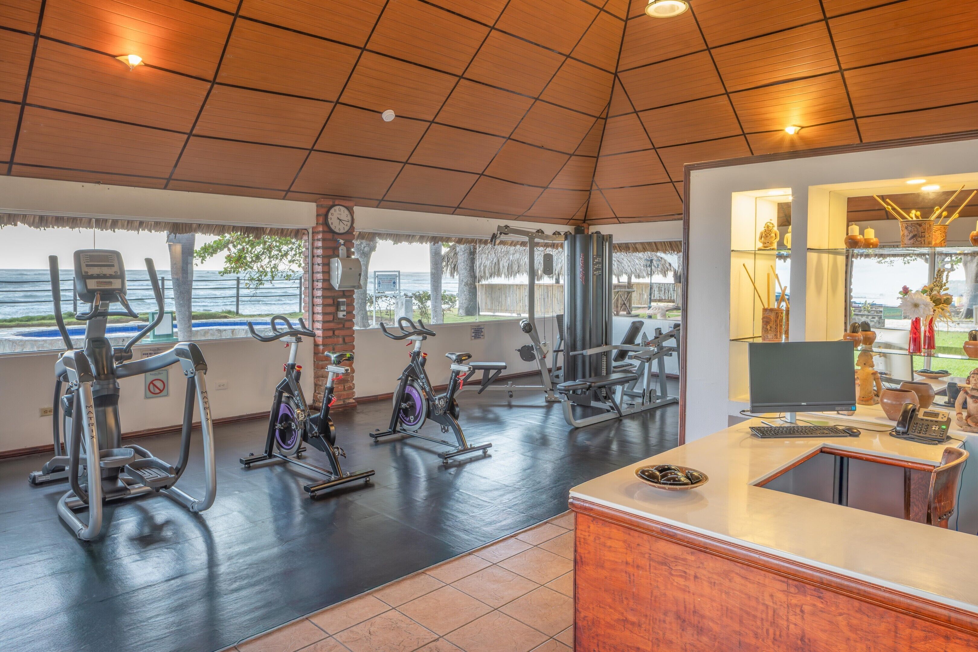 Un gimnasio con equipamiento de ejercicio, una recepción y vista al océano.