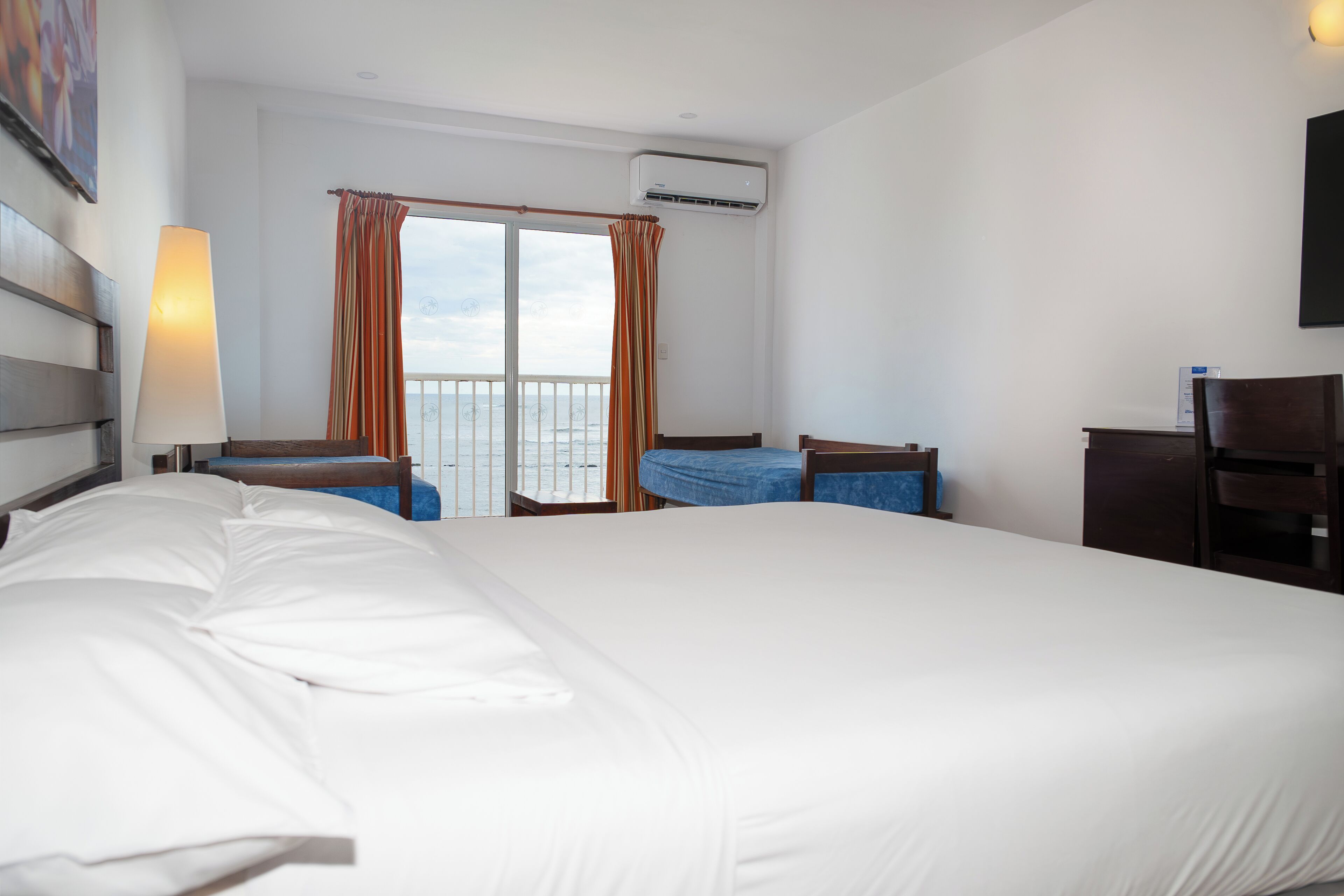Ein Hotelzimmer mit einem großen Bett, einem Schreibtisch, einem Stuhl, einer Lampe und Blick auf den Balkon.
