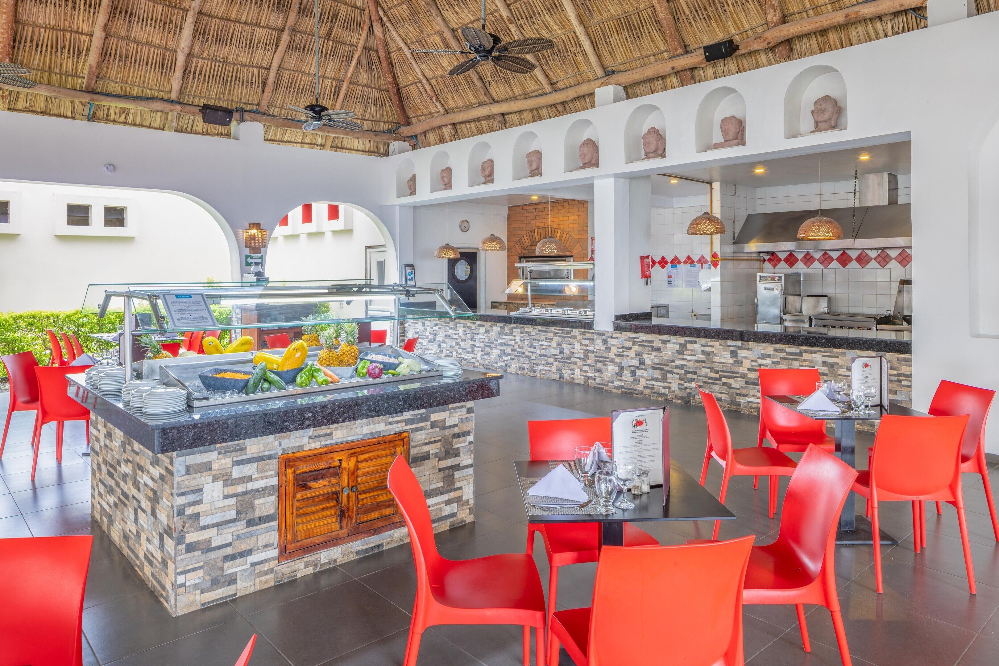 A restaurant with a central island, red chairs, and a kitchen area.