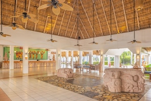 A spacious lobby with a thatched roof, stone sculptures, and a reception area with artwork.