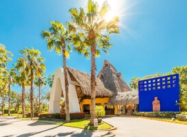 Un resort con un edificio de techo de paja, palmeras y un muro azul con una estatua.