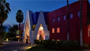 Un edificio moderno con una fachada geométrica distintiva, que presenta una entrada central con una cubierta de vidrio.