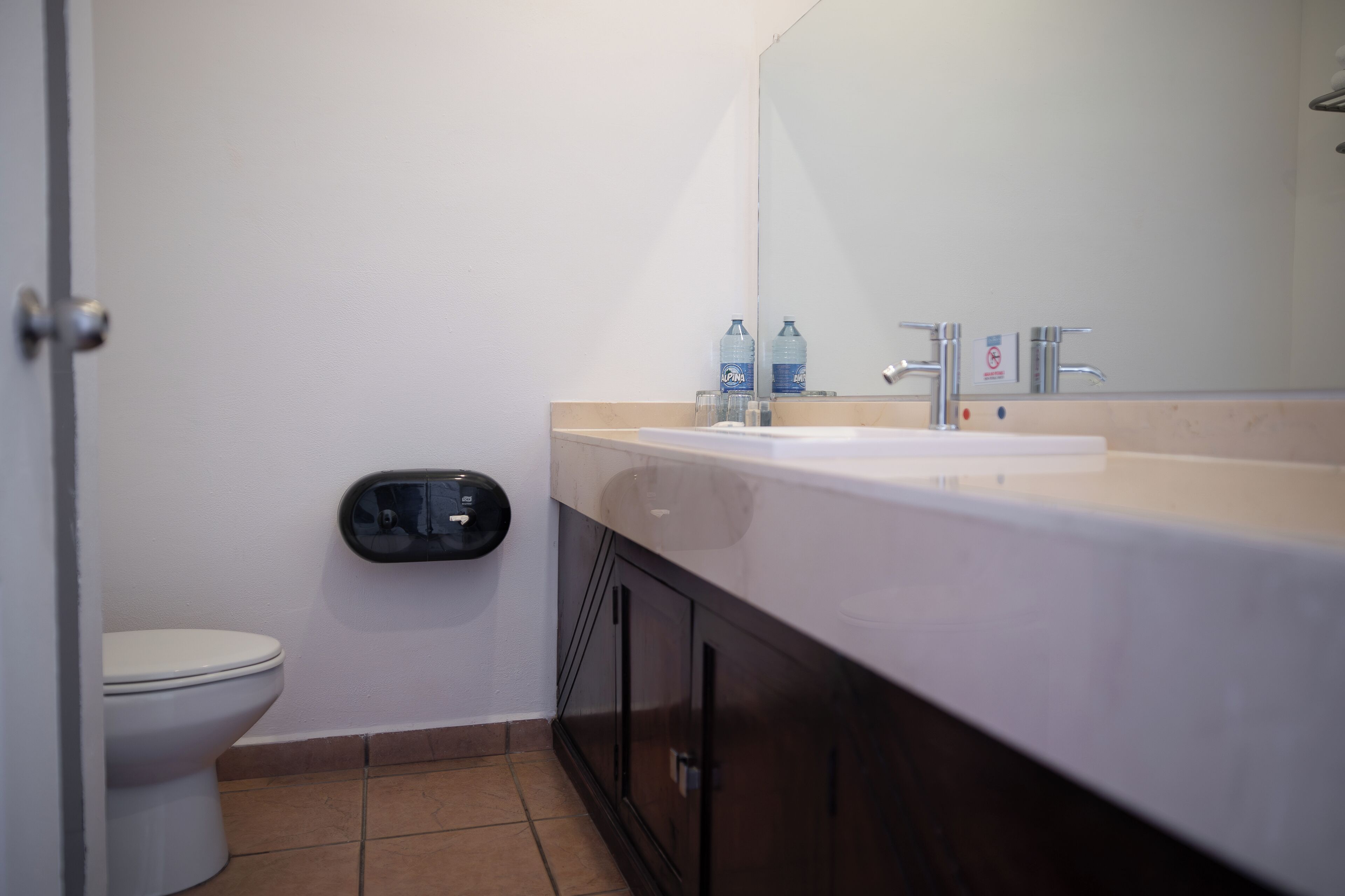 A bathroom with a white toilet, a sink with a mirror, and two bottles of water on the counter.
