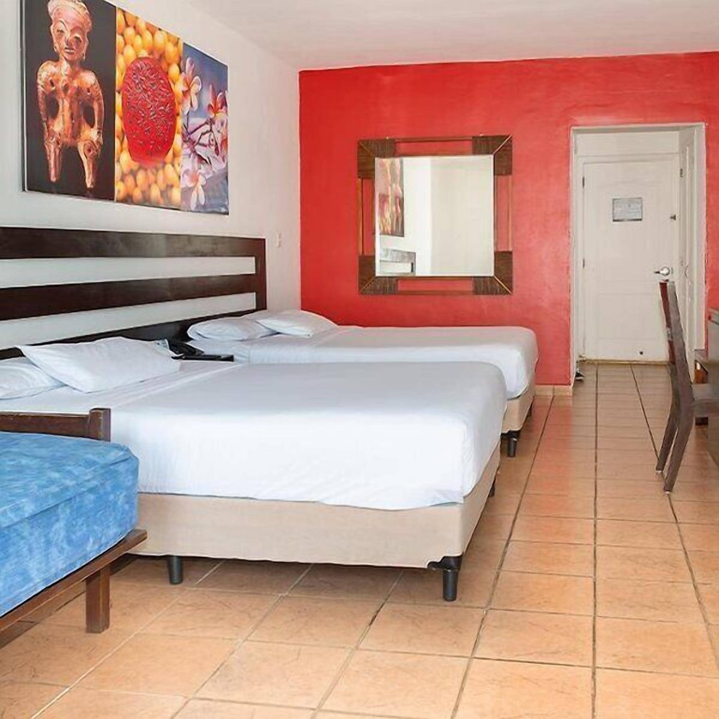 Een hotelkamer met twee bedden, een rode accentmuur, een spiegel en een deur.